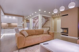 Luxurious living room with modern interior design, featuring beige sofa, fireplace, and open kitchen.