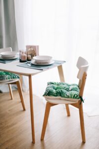 Contemporary dining room with wooden furniture and green-leaf cushions. Bright and inviting.