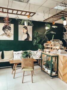 Stylish café interior featuring modern décor, green walls, plants, and comfortable seating.