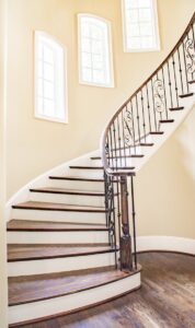 Beautiful spiral staircase with iron railings and wooden steps, lit by natural light.