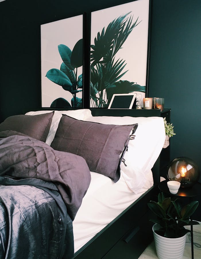 A stylish and cozy bedroom featuring green walls, botanical prints, and soft lighting for a contemporary feel.